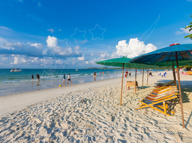 White sand beach with green and blue umbrellas, striped deck chairs, distant swimmers and boats under blue sky