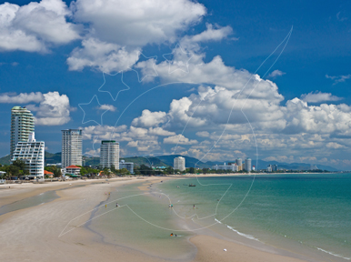 Curving white sand beach with shallow turquoise water and distant high-rise hotels under towering cumulus clouds