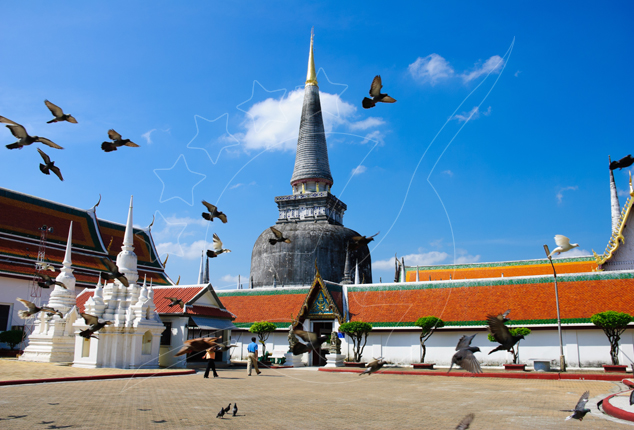 Tall dark chedi and orange-tiled temple halls at a Thai Buddhist temple with pigeons flying under a blue sky