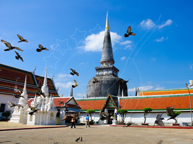 Pigeons flying over a tall golden-spired chedi and white stupas at a Thai Buddhist temple under blue sky