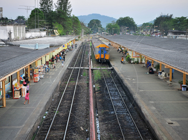 Elevated view of a tropical railway station with two covered platforms, tracks and an orange diesel locomotive