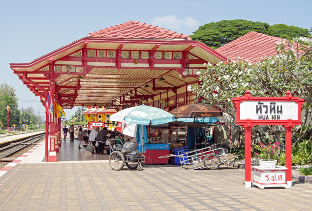 Red and cream Thai pavilion platform at Hua Hin railway station with vendor stalls and bilingual station sign