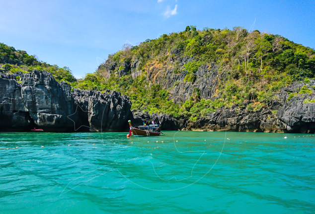 Longtail boat moored in turquoise water beside jungle-covered limestone cliffs under a blue sky