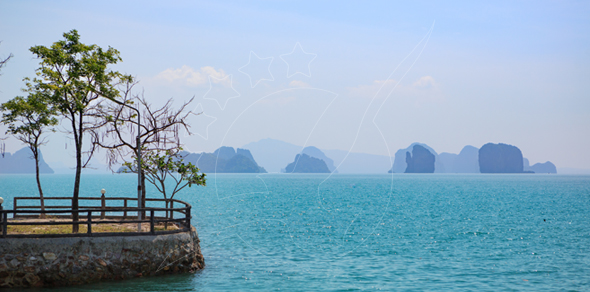 Turquoise sea view from a stone pier with railing and trees, limestone karst islands hazy on the horizon