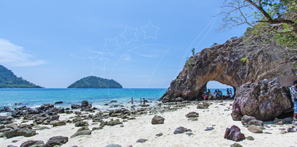 Limestone rock arch on a white sand beach with turquoise sea, distant green island and small groups of visitors