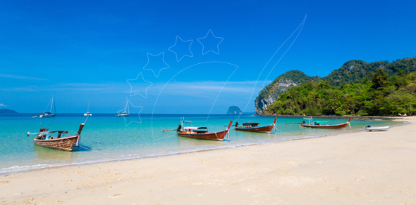Wooden longtail boats moored on a white sand beach with turquoise water, limestone karst headland and distant sailboats