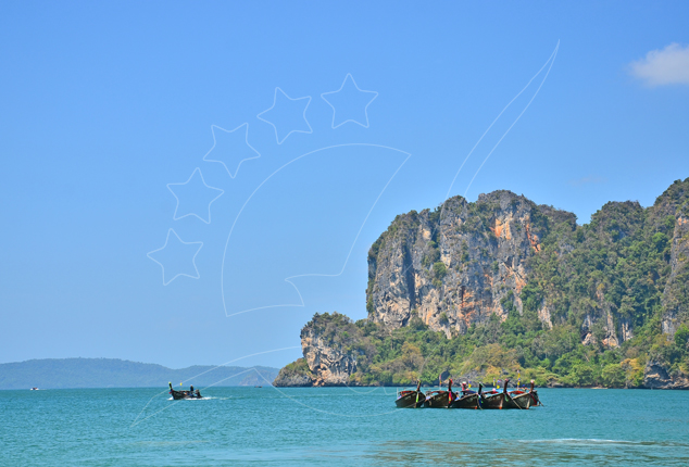 Longtail boats moored off a limestone karst headland in turquoise Andaman Sea water under clear blue sky