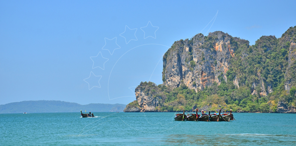 Longtail boats moored beside towering limestone karst cliffs in turquoise water under clear blue sky