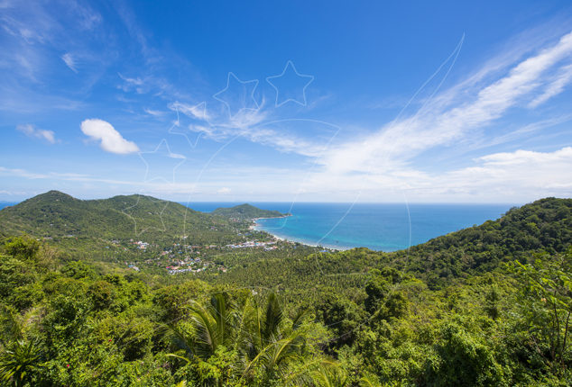 Hilltop view over jungle-covered hills to a curving bay, coastal village and turquoise sea under blue sky