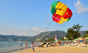 Colourful parasail canopy inflating on a busy tropical beach with sun loungers and forested headland behind