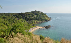 Small sandy cove framed by forested headland and rocky outcrops on a turquoise tropical sea