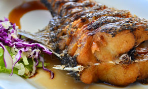 Close-up of deep-fried whole fish glazed with dark sauce on a white plate beside shredded purple cabbage salad