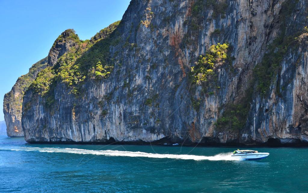Speedboat racing past towering limestone cliffs over turquoise water, likely Phi Phi, Thailand