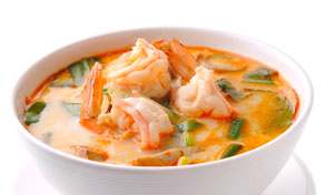 Bowl of creamy Thai tom yum goong soup with prawns, mushrooms and spring onion on white background