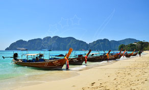 Row of Thai longtail boats moored on a white sand beach with turquoise water and limestone hills behind