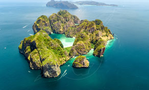 Aerial view of forested limestone islands ringed by turquoise lagoons and small boats in a deep blue sea