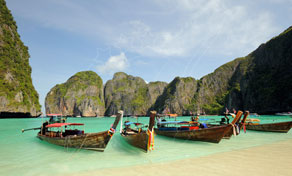 Longtail boats moored in turquoise shallows of a limestone cliff bay with pale sand beach, Thailand