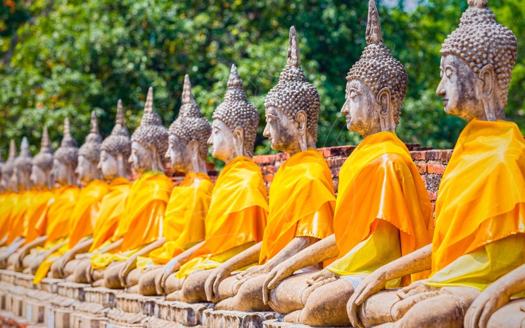 Row of seated stone Buddha statues draped in orange saffron robes at an Ayutthaya temple, Thailand