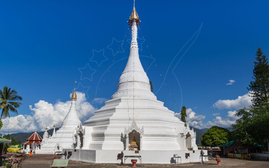 White Buddhist chedis with golden spires at Wat Phra That Doi Kong Mu hilltop temple under blue sky, Thailand