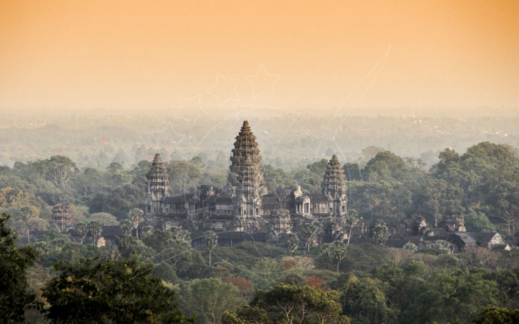 Angkor Wat temple towers rising above misty jungle canopy at hazy sunrise