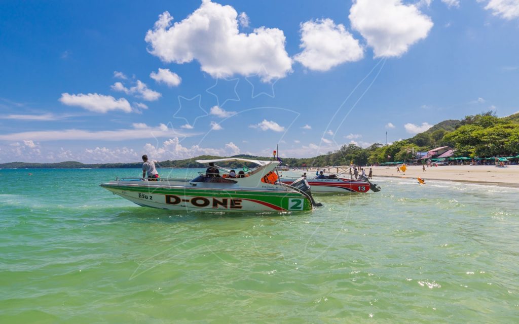 Two speedboats moored in turquoise shallow water off a tropical beach with tourists and umbrellas onshore