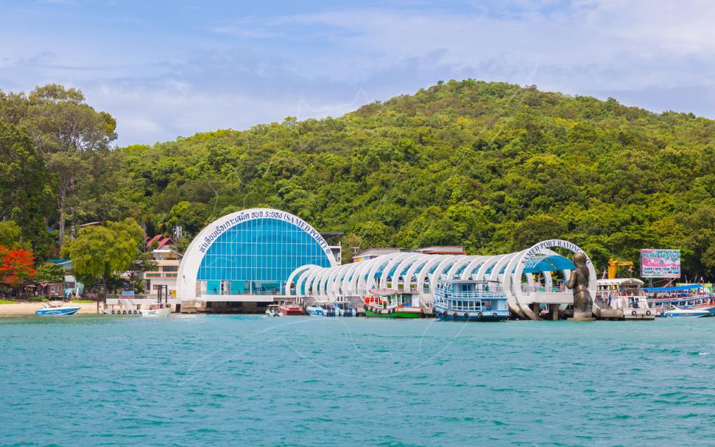 Samed Port pier in Rayong, Thailand, with white arched walkway, moored ferries and turquoise sea below a green hill