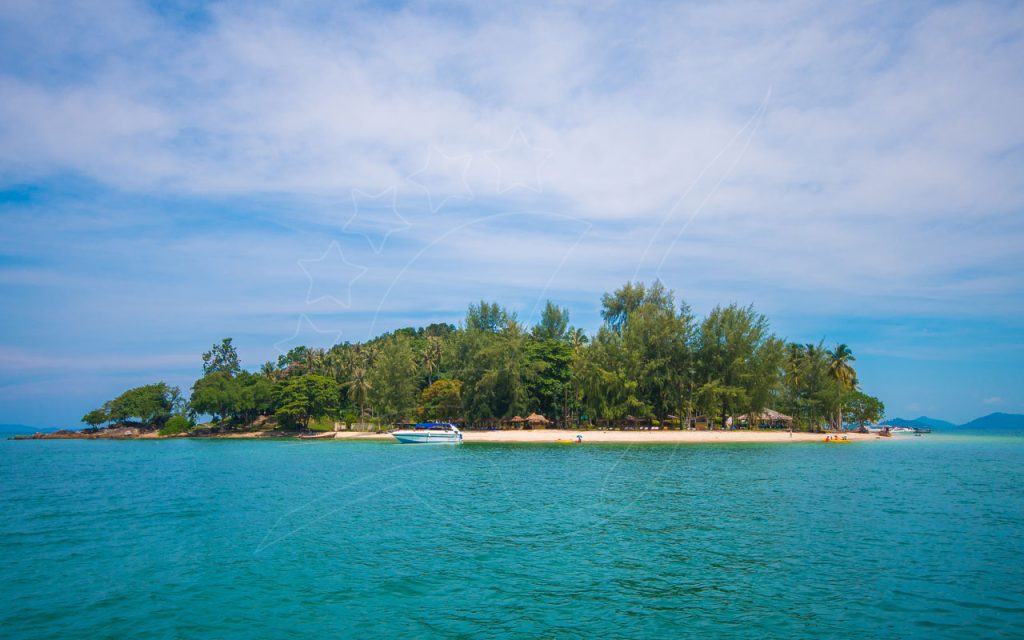 Small tropical island with dense green trees, white sand beach, moored speedboat and kayaks in turquoise sea