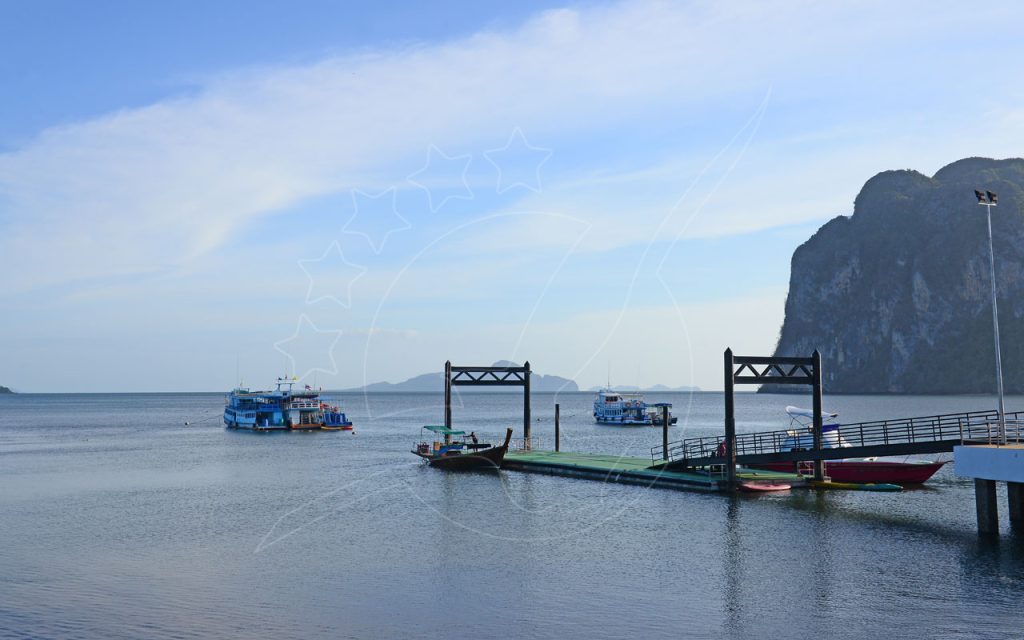 Floating pier with longtail boat and kayaks, ferries anchored offshore beside a limestone karst headland at dawn