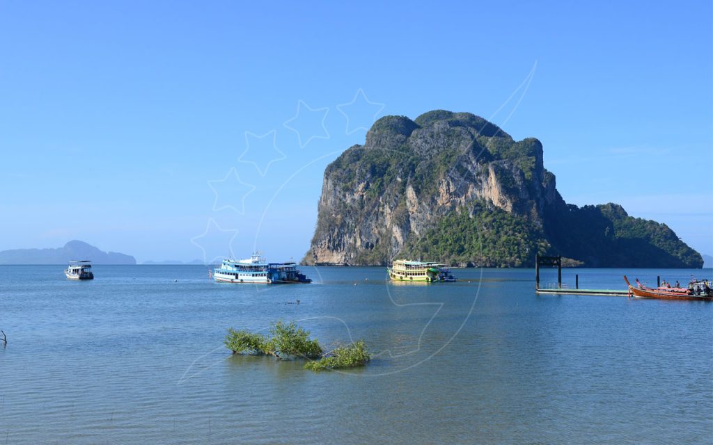 Limestone karst island over calm blue sea with passenger ferries, longtail boats and a concrete pier