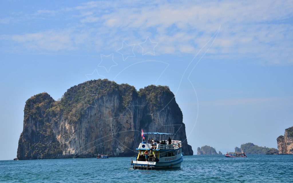 Wooden dive boat with passengers anchored beside a towering limestone karst island in calm turquoise sea