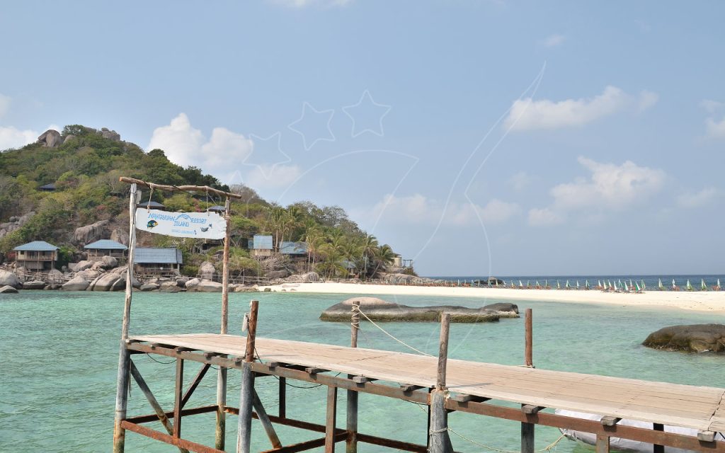 Wooden pier with Nangyuan Island Dive Resort sign facing turquoise water, white sandbar and hillside bungalows