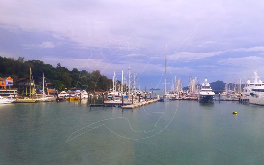 Yachts and sailboats moored at a tropical marina with jetties, forested hillside and calm green water