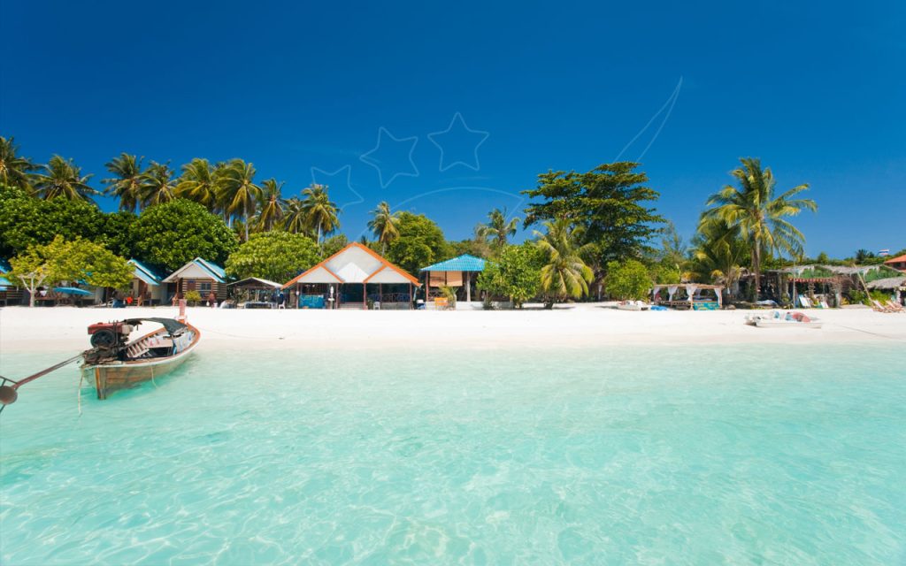 Wooden longtail boat moored in clear turquoise shallows off a white sand beach lined with palms and bungalows