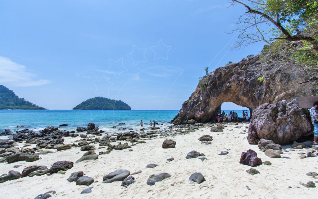 Tropical beach with rocky arch, turquoise sea, distant islands and tourists under a clear blue sky