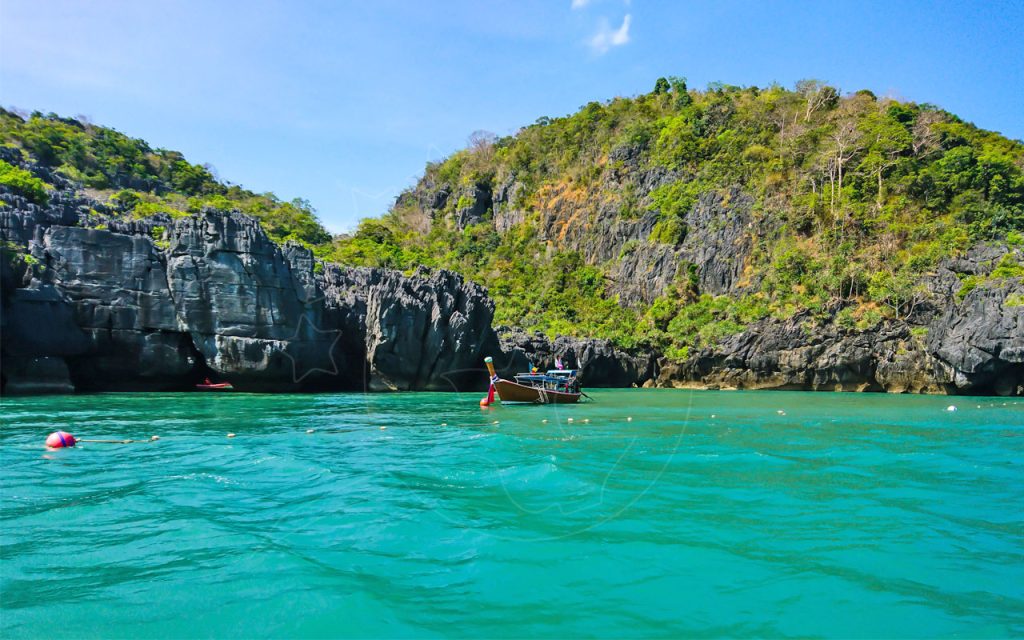 Wooden longtail boat moored beside limestone cliffs in a turquoise lagoon under blue sky