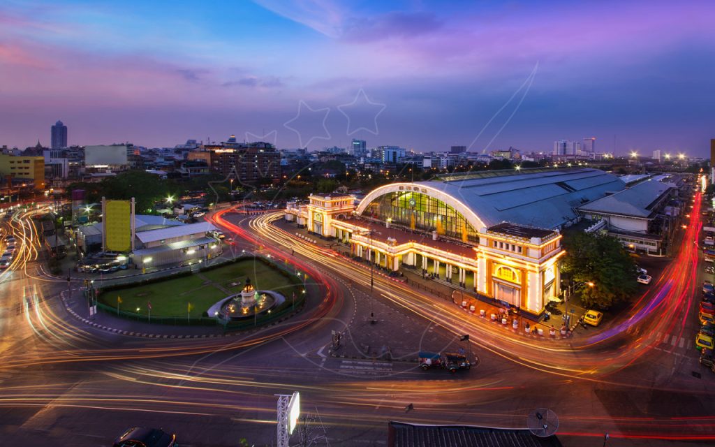Illuminated Hua Lamphong railway station in Bangkok at twilight with car light trails circling a fountain roundabout