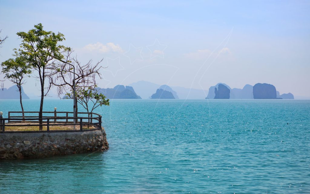 Stone viewpoint terrace with wooden railing and trees beside turquoise sea, limestone karst islands on horizon