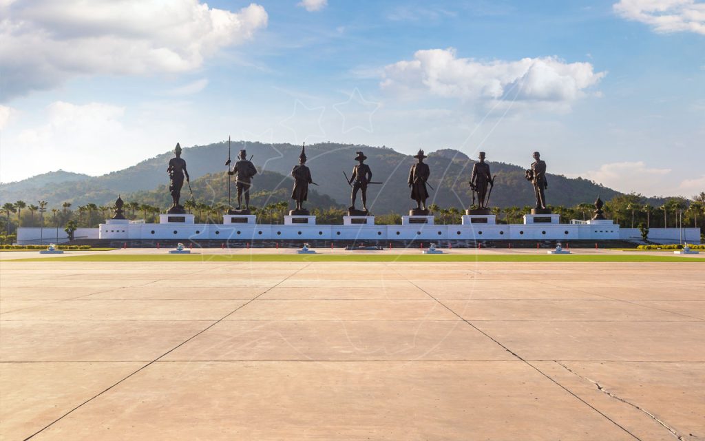 Seven bronze royal statues on a white plinth wall at Rajabhakti Park, Hua Hin, with green hills behind