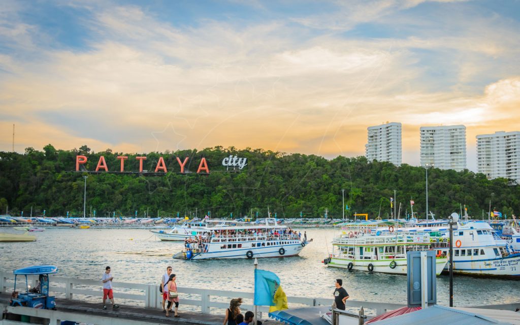 Passenger ferries at Bali Hai Pier, Pattaya, with hillside PATTAYA city sign, tourists on walkway and condo towers at sunset