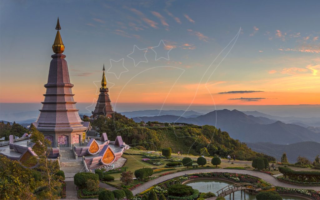 Twin royal pagodas with golden spires on a mountain ridge at Doi Inthanon, Thailand, above misty hills at sunset