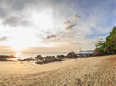 Sunset over a quiet tropical beach with volcanic rocks, golden sand and a small boat offshore