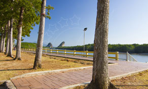 Tree-lined brick riverside promenade with white guardrail, calm river and limestone karst hills under clear blue sky