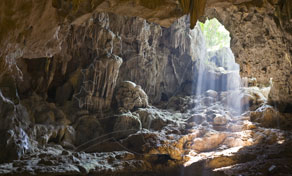 Sunlight streaming through an opening into a limestone cave with rock formations and stalactites
