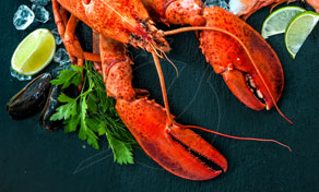 Cooked red lobster with claws on dark slate, garnished with parsley, lime wedges, mussels and ice