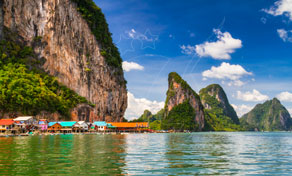 Stilt-house floating village with red roofs beneath towering limestone karst cliffs on turquoise bay water, Thailand