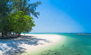 Tropical beach with white sand, turquoise shallow water and shade trees under a clear blue sky