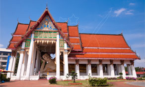 Thai Buddhist temple hall with tiered orange tile roof, white columns and gilded gable under blue sky