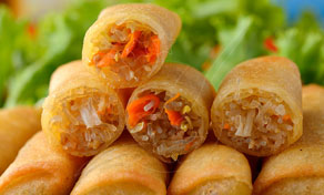 Stack of golden fried spring rolls, some halved to show vegetable and noodle filling, on green lettuce