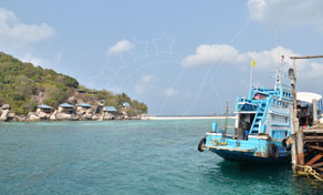 Blue wooden fishing boat moored at a concrete pier beside a green tropical island and turquoise sea