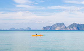 Two paddlers in an orange kayak on calm turquoise sea with limestone karst islands on the horizon